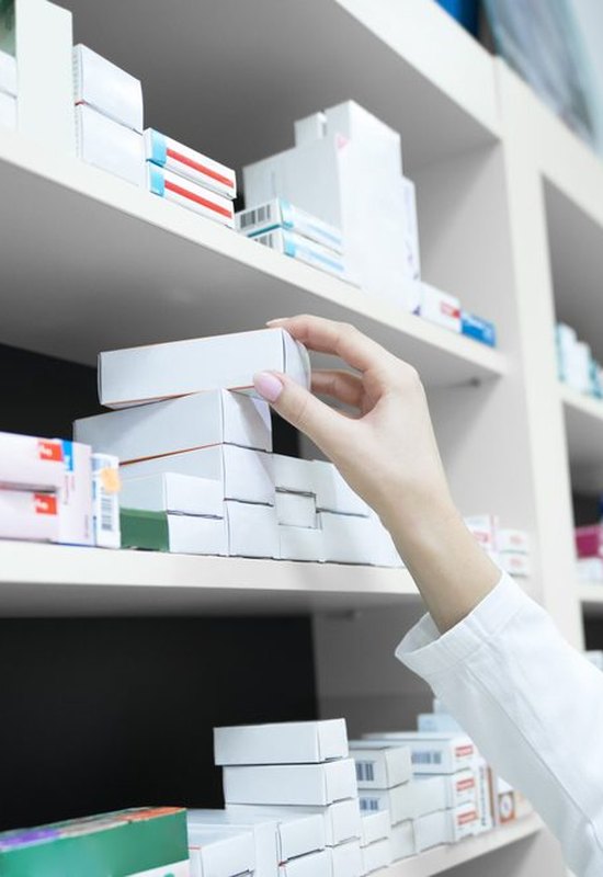 Farmacéutica cogiendo un medicamento de la estantería